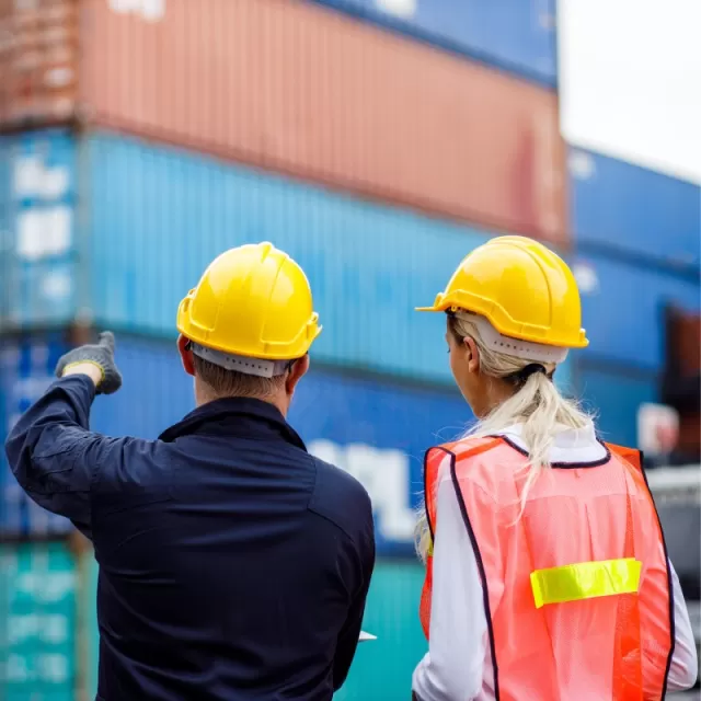 Two port workers with hard hats looking at stacked international shipping containers
