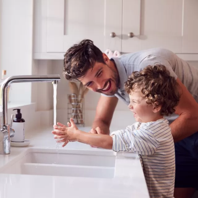 Father and son playing with clean water from tap at kitchen sink